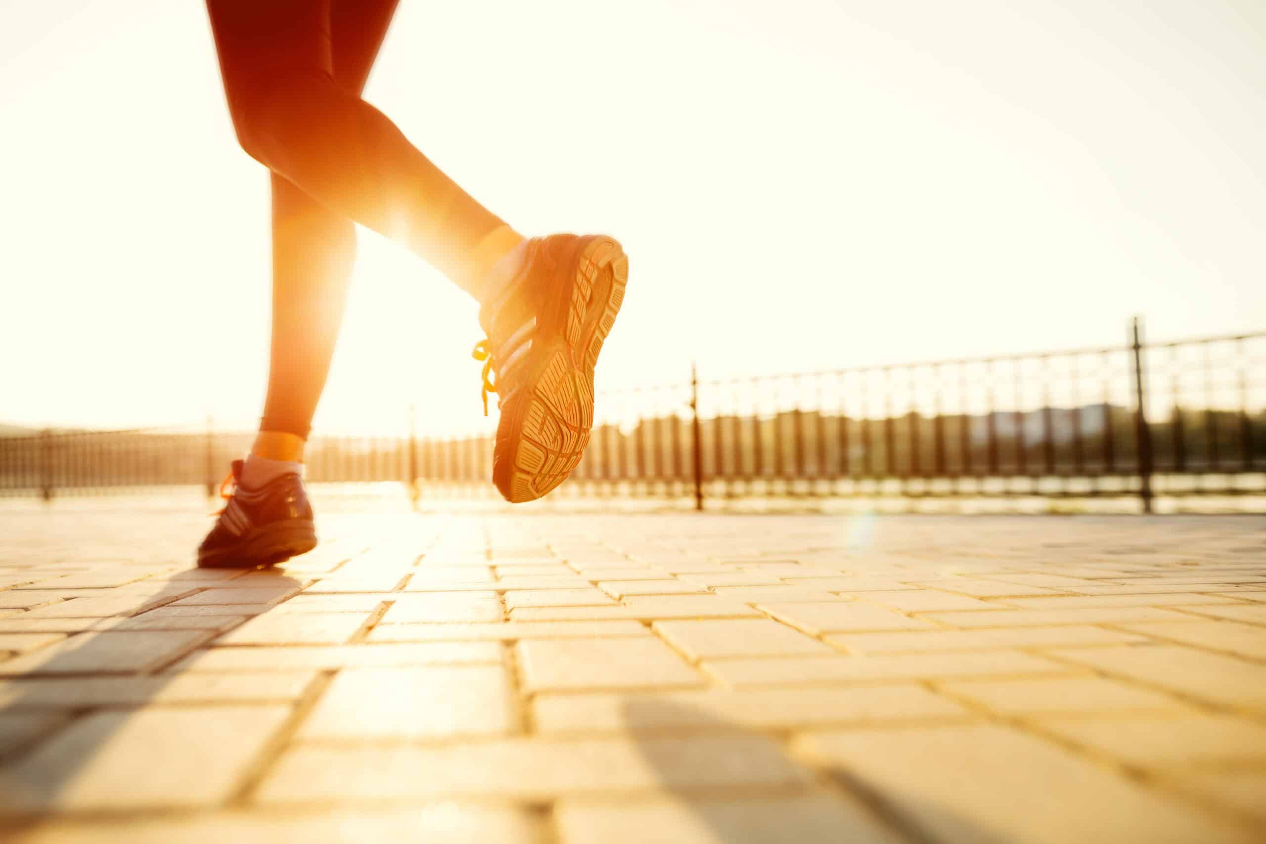 Runner's shoe mid-step on sunlit brick pavement with a fence in the background, warm sunset glow